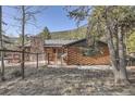 Cozy log cabin-style home with a stone chimney and fenced yard surrounded by trees at 10439 Christopher Dr, Conifer, CO 80433
