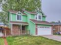 Green home with a two-car garage and partial brick facade at 12025 Monaco Dr, Brighton, CO 80602