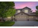 Charming home featuring a brick and siding exterior, three-car garage, manicured lawn, and mature tree under a sunset at 989 Graland Pl, Highlands Ranch, CO 80126