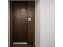 Hallway view of a dark wood-finished unit door with a silver handle and room number 