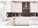 Well-lit kitchen with white cabinets, stainless steel appliances and dark backsplash at 20411 E 53Rd Ave, Denver, CO 80249