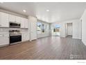 Open-concept kitchen with stainless steel appliances, white cabinets, and wood-look flooring at 2263 Serenidad St, Brighton, CO 80601