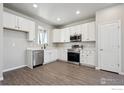 Well-lit kitchen with white cabinets, stainless steel appliances, and wood-look floors at 2263 Serenidad St, Brighton, CO 80601