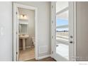 Bright entryway featuring a modern door and a glimpse into a half bathroom with pedestal sink and tile floors at 2283 Serenidad St, Brighton, CO 80601