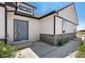 Front entrance with gray door, stone accents, and landscaping at 16474 Essex S Rd, Platteville, CO 80651