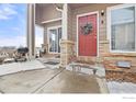 Red front door, brick porch, grill, and snowy landscaping at 1601 Great Western Dr # G8, Longmont, CO 80501