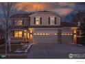 Two-story house with a beige exterior, a three-car garage, and a manicured lawn at dusk at 1420 Hickory Dr, Erie, CO 80516