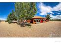 Log cabin featuring a bright red door and windows, surrounded by mature trees and expansive gravel landscape at 2244 County Road 12, Erie, CO 80516