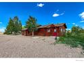 Log home with red doors, complemented by mature trees and gravel landscaping under a brilliant blue sky at 2244 County Road 12, Erie, CO 80516