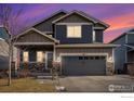 Two-story house with gray siding, stone accents, and a two-car garage at dusk at 344 Ellie Way, Berthoud, CO 80513