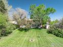 Spacious backyard with a well-manicured lawn, mature trees, and an outdoor fireplace at 4667 Ashfield Dr, Boulder, CO 80301