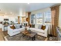 Open living room with white sofas, a wood coffee table, and large windows at 889 Crest St, Lochbuie, CO 80603