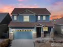 Charming two-story blue home at dusk featuring a covered front porch, two car garage and landscaped front at 1417 Bluemoon Dr, Longmont, CO 80504