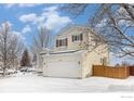 Side view of charming two-story home with a two-car garage and wooden fence in winter at 1577 Bain Dr, Erie, CO 80516