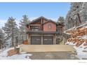 Charming exterior view of a home with stone accents, a two-car garage, and surrounding snowy trees at 795 Pine Brook Rd, Boulder, CO 80304