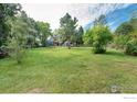Large backyard featuring a lush lawn, mature trees, and a glimpse of the home's deck and upper balcony at 6146 S Fulton St, Englewood, CO 80111