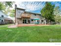 Expansive backyard with lush green lawn, mature trees, a large deck with patio furniture, and a second story balcony at 6146 S Fulton St, Englewood, CO 80111