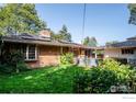 Lush backyard featuring brick exterior, with vibrant green lawn, mature trees, and a privacy fence at 390 Inca Pkwy, Boulder, CO 80303
