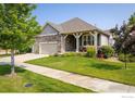 Inviting exterior view of a home featuring a well-kept lawn, mature trees, and a charming front porch at 13943 W 87Th Ln, Arvada, CO 80005