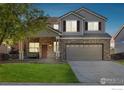 Dusk view of a two-story home featuring a brick facade, manicured lawn, and an inviting covered front porch at 14828 E 118Th Pl, Commerce City, CO 80603