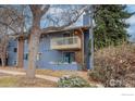 Two-story blue condo with a balcony, patio, mature trees, and sparse winter landscaping at 2800 Kalmia Ave # 320, Boulder, CO 80301