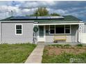 Charming home exterior featuring gray siding, solar panels, covered porch with a yellow bench, and a green roof at 98 N 12Th Ave, Brighton, CO 80601