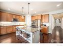 Modern kitchen featuring a large center island, stainless steel appliances, wood cabinets, and stylish pendant lighting fixtures at 12596 Eagle River Rd, Firestone, CO 80504