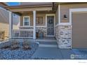 Inviting front porch featuring stone accents, a decorative wreath and stylish outdoor lighting at 1141 Blue Bell Rd, Berthoud, CO 80513