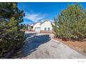 Exterior view of home's driveway, framed by mature pine trees and tidy landscaping at 16498 S Essex S Rd, Platteville, CO 80651