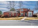 Traditional brick home featuring manicured lawn, mature trees, sidewalk and driveway with a gray roof at 664 Manorwood Ln, Louisville, CO 80027