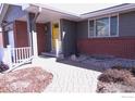 Inviting front porch with brick accents, a yellow door, and well-maintained landscaping at 2996 S Lamar St, Denver, CO 80227