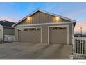 Two-car garage with neutral siding, multiple windows and lighting, with white fencing and a large concrete driveway at 636 Morrison Dr, Frederick, CO 80530