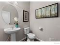 Half bathroom with pedestal sink, round mirror, and decorative wall art at 2405 Horse Shoe Cir, Fort Lupton, CO 80621