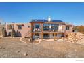 Expansive rear view of home with large deck, patio and lush lawn; Solar panels above and stone landscaping at 11251 Lookout Dr, Longmont, CO 80504