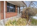 A cozy brick-clad front porch, with a low wall, and a welcoming entrance to the home at 1735 S Kline Way, Lakewood, CO 80232