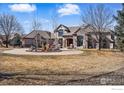 The home features stone accents, mature trees, and a circular driveway with water feature at 8733 Portico Ln, Longmont, CO 80503