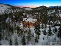 Expansive aerial view of a luxurious mountain home surrounded by snow-covered trees and a mountain range at 500 Highfield Trl, Breckenridge, CO 80424