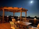 Outdoor dining area on a deck with city light views at night under a wood pergola at 15757 Mossrock Ct, Longmont, CO 80503