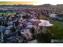 Scenic aerial view of a community with a golf course, pond, lush trees, and mountain backdrop at 567 Manorwood Ln, Louisville, CO 80027