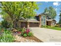 Charming home with a large front yard featuring a mature tree, colorful flower beds, and a spacious three-car garage at 567 Manorwood Ln, Louisville, CO 80027