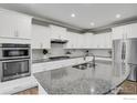 Modern kitchen features stainless appliances, a granite countertop island with a sink, and plenty of white cabinet storage at 9968 E Kansas Ave, Aurora, CO 80247
