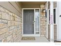 Close-up of the front door with stone accents, a glass side panel, and a welcoming doormat at 12597 Eliot St, Broomfield, CO 80020