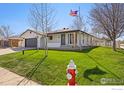 Inviting single-story home featuring a green lawn, American flag, and a charming covered porch with brick columns at 1643 Vivian St, Longmont, CO 80501