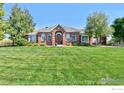 Beautiful brick home boasts a well-manicured lawn, elegant arched entryway, and mature shade trees at 18399 Wagon Trl, Mead, CO 80542