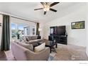 Inviting living room featuring plush sofas, a ceiling fan, and large windows offering abundant natural light at 1002 Stage Dr, Fort Lupton, CO 80621
