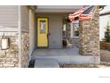 Inviting front porch with a yellow door, stone accents and a cozy chair to sit and relax on at 117 Nova Ct, Erie, CO 80516
