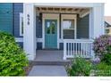 Welcoming front porch with teal door, white pillars and a decorative railing, surrounded by flowering bushes and greenery at 658 Casper Dr, Lafayette, CO 80026