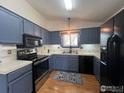 Galley kitchen featuring updated stainless steel appliances, blue cabinets and a window above the sink at 1406 Oak Dr, Berthoud, CO 80513