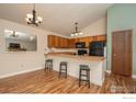 Eat-in kitchen features wood cabinets, black appliances, breakfast bar with seating and wood-look flooring at 373 Fir Ln, Broomfield, CO 80020