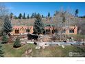 Expansive view of the home exterior featuring a stone patio, pool and mature trees on a sloping lot at 136 Old Post Office Rd, Boulder, CO 80302